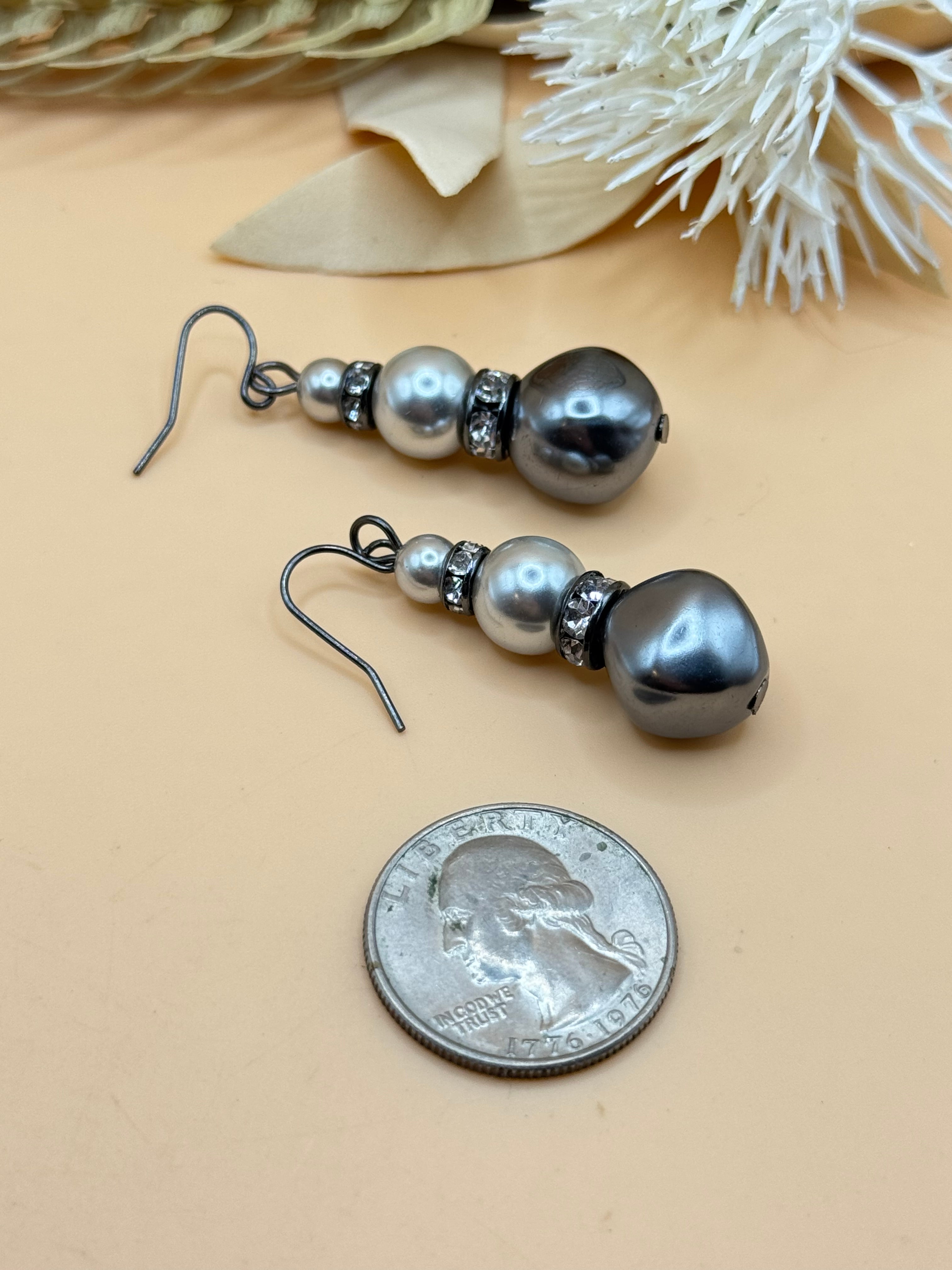 Elegant pierced earrings featuring round faux pearl studs with elongated faux pearl teardrop dangles. Gold tone accents add a classic, polished finish.