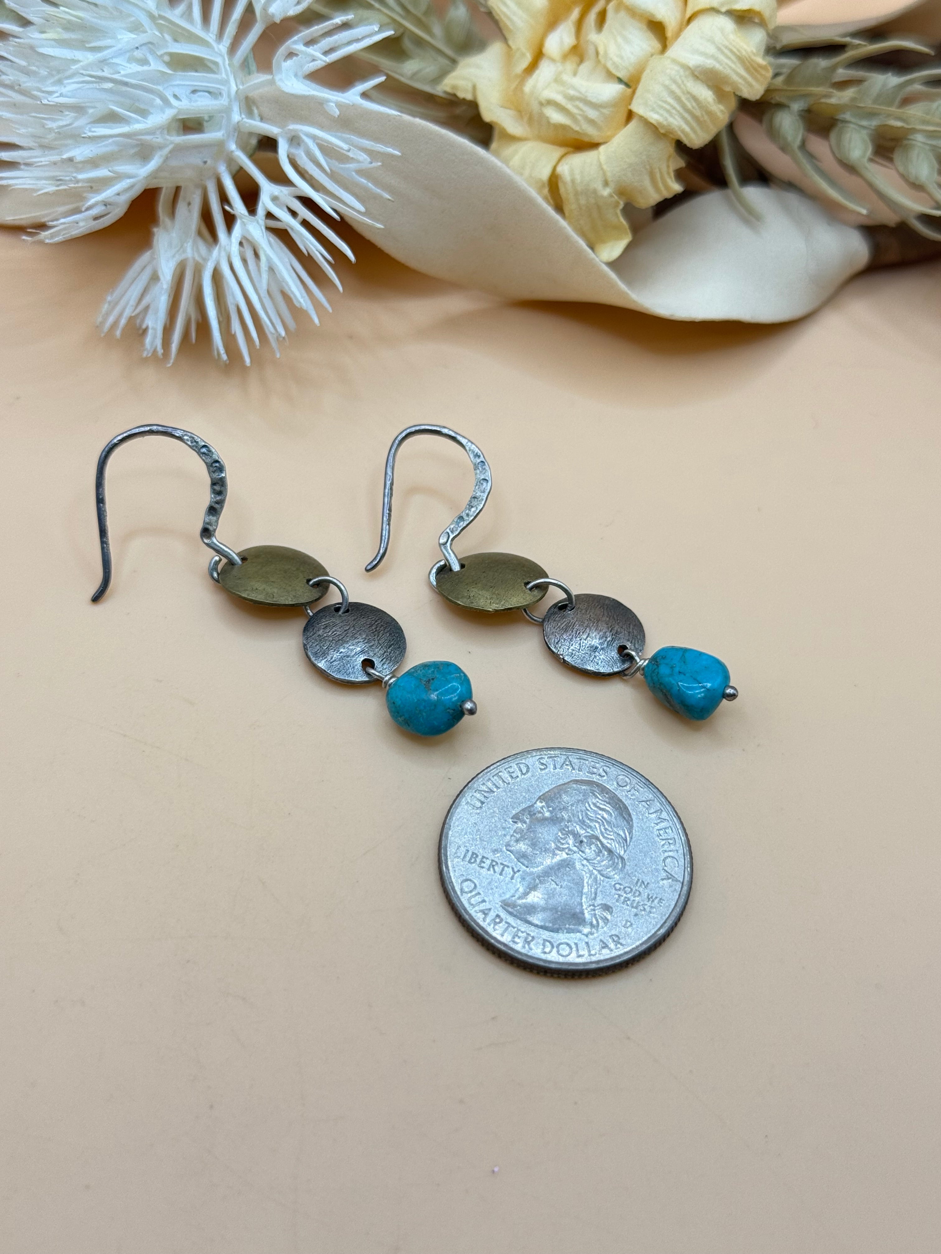 Artisan mixed metal dangle earrings featuring brass and silver tone disc accents with vibrant turquoise nugget beads. Their handcrafted boho style makes them a unique accessory for everyday wear or Southwestern-inspired looks.