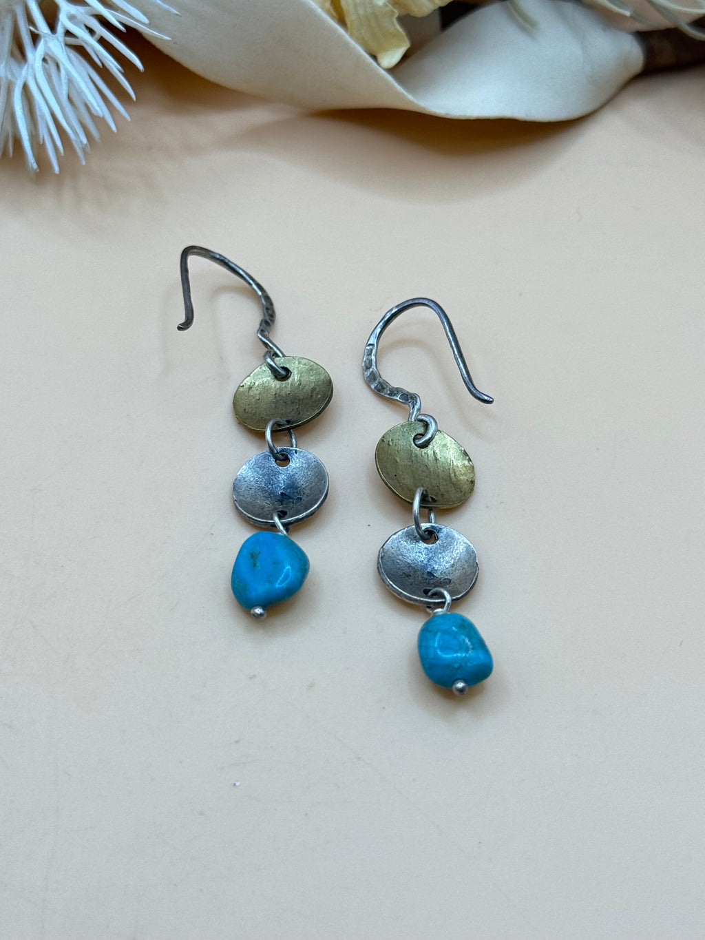 Artisan mixed metal dangle earrings featuring brass and silver tone disc accents with vibrant turquoise nugget beads. Their handcrafted boho style makes them a unique accessory for everyday wear or Southwestern-inspired looks.